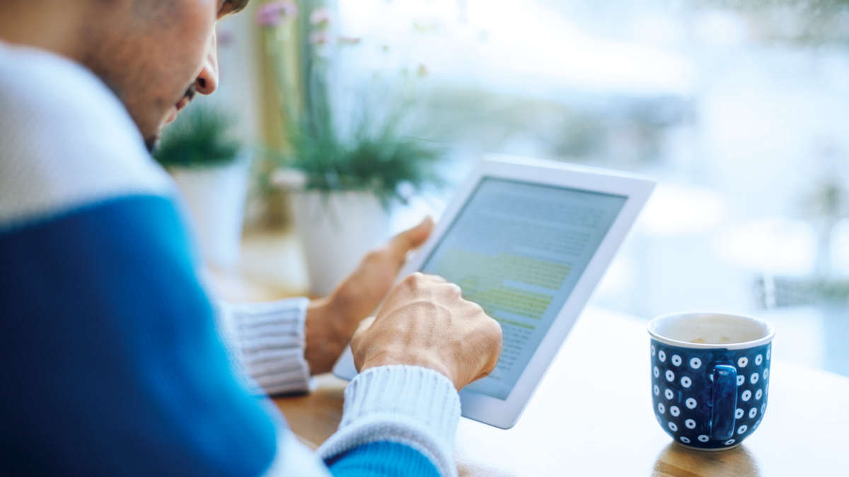 winter, male person reading an ebook in front of a window with coffee cup
